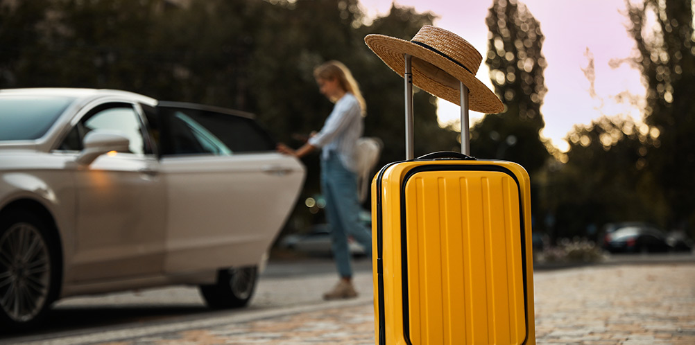 In focus yellow suitcase with woman in background opening taxi door